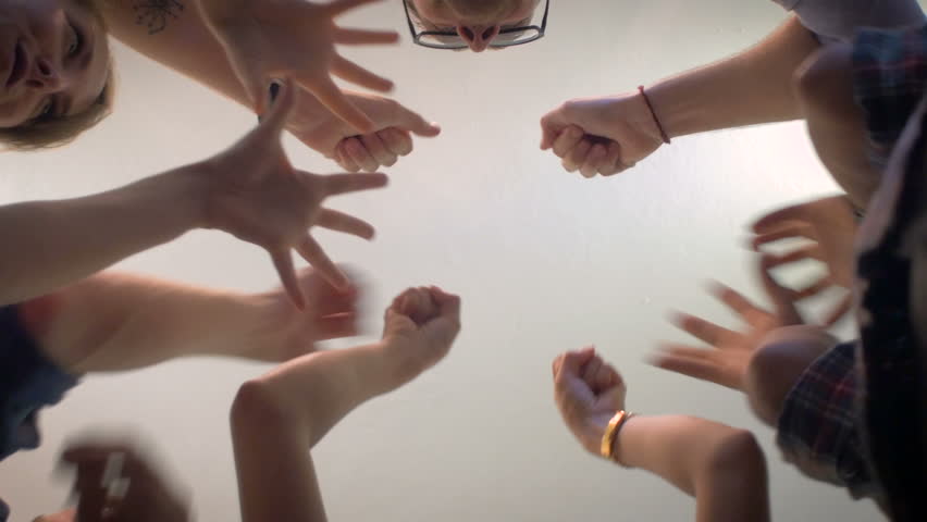 Low angle shot from below of a group of 5 young millennials place their hands together in the center of a circle and then cheer in a celebration of a successful event and shake hands and fist bump. Royalty-Free Stock Footage #11970596