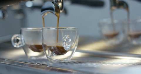 Slider of hot espresso coffee pouring into a two transparent cups from coffee machine in 4k (close up)