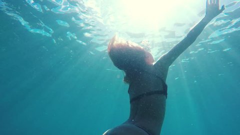 Woman in Bikini swimming underwater towards surface with beautiful sun flares in slow motion. Instagram Color Tone