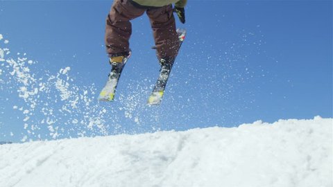 SLOW MOTION CLOSE UP: Freestyle skier jumping big air kicker in snowy mountains in sunny winter