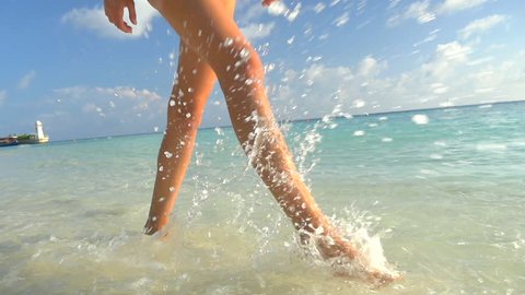 SLOW MOTION CLOSE UP: Young female with long legs walking on exotic sandy beach in Maldives and spraying the sea water into the camera