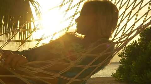 SLOW MOTION: Woman lying in hammock on beautiful exotic beach at golden sunset in paradise Maldives island