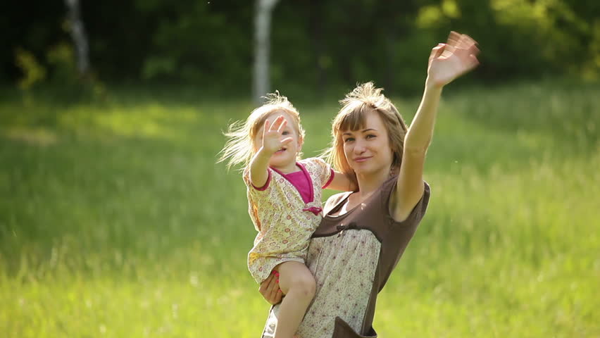 Happy mother and child waving hands in the park 