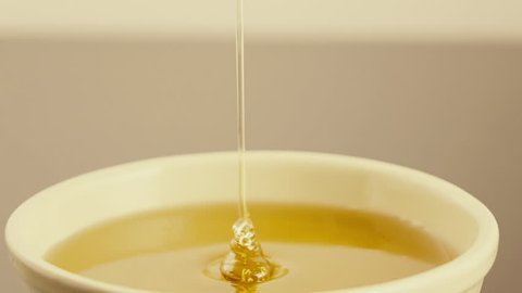 Honey pouring from dipper to bowl slow motion tilt down.100fps-25fps slow motion close up tilt down shot of honey dripping from a dipper,on to a bowl filled with honey.
