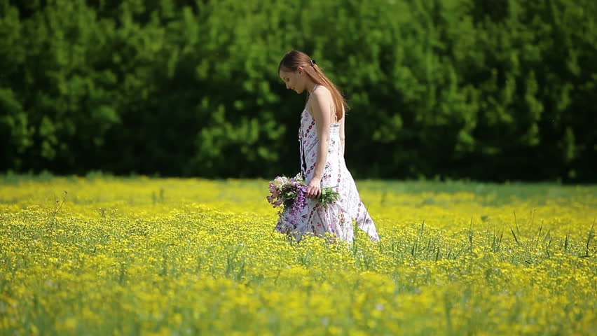 Beautiful young adult lady in the meadow with flower in hand 