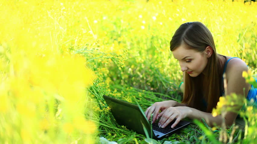 Young lady with laptop in the grass. Tripod pan. 