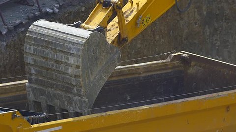Slow Mo. Dump truck being loaded with soil by shovel. Close up, original HD video. Construction machinery working at the construction site
