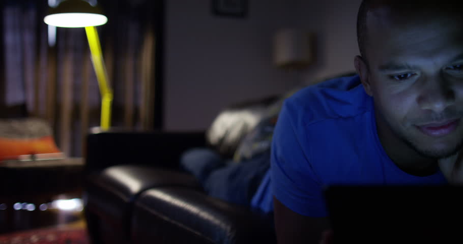 An attractive young man streaming a movie on his digital tablet. Shot on RED Epic.
