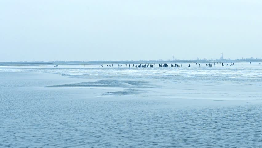 Partly frozen water storage basin on Dnieper river in Vyshgorod near Kiev, Ukraine, with many winter fishermen angling on ice on background of breakwater and transmission towers far off