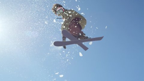 SLOW MOTION CLOSEUP: Freestyle skier jumping big kicker and flying over the sun in snowy mountains