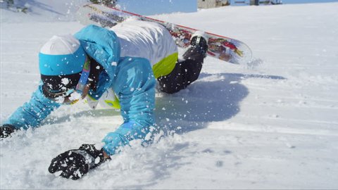 SLOW MOTION CLOSE UP: Snowboarder riding and falling on ski slope in sunny ski resort