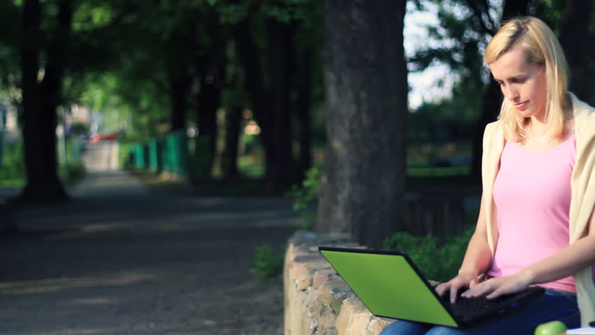 Attractive female student working on laptop in the park, dolly shot 