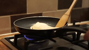 4K caucasian hand with spatula pushes pancake around a pan. A 4K clip of a caucasian female hand with a wooden spatula pushes a white pancake around a frying pan. The heat is on!