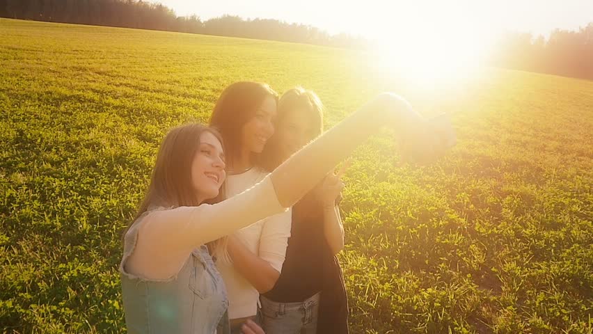 Three friends, young pretty girls, caucasians, having fun outdoors in nature, walking, making selfie, laughing, fooling around, slow motion.
