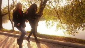 Two friends, young pretty girls, caucasian and african, having fun outdoors in park, walking, talking, laughing, fooling around, slow motion.