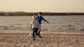two little boys playing football on the beach of the lake at sunset