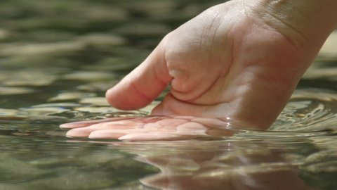 SLOW MOTION CLOSEUP: Hand grabbing and lifting crystal clear water in mountain spring, drops dropping into the water surface