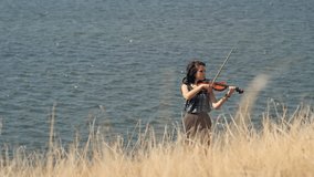Young woman on the mountain playing the violin on sea background