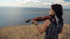 Young woman on the mountain playing the violin on sea background. Steadicam shot