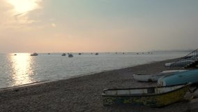 Beach sunset with boats on the water as well as on land. The sun is low in eh west and casting a reflection on the glistening water. This clip was filmed at Southend, UK.