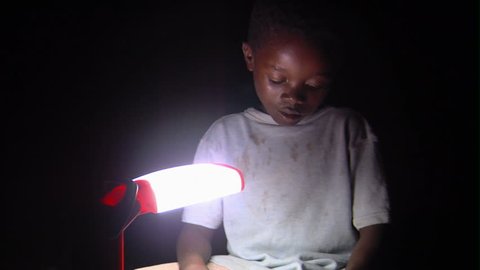 Kenya, Africa - April, 2013: Medium shot of child reading by lamp