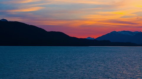 Traveling time lapse shot of a beautiful yellow/ orange sunset behind the silhouette of a mountain ridge. You can see a snow covered mountain along the horizon. June 3rd, 2009 near Haines, Alaska.