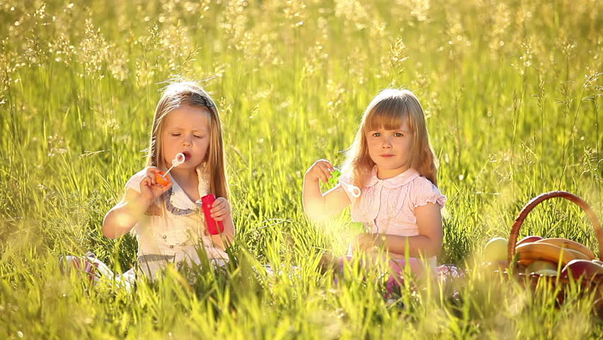 Two little girls in the meadow. Blow bubbles. 