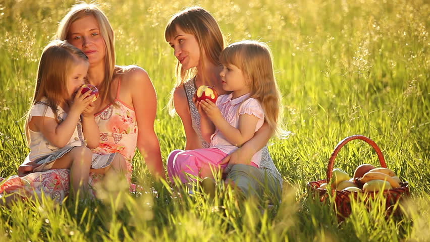 Two mothers with daughters in the field. Kids eating apples. 