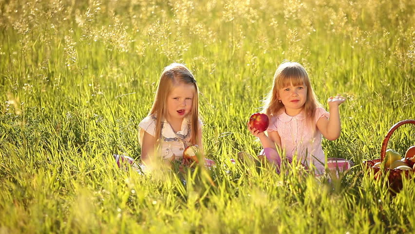 Two sisters eating apples in the meadow. Beside a basket of apples - 2 
