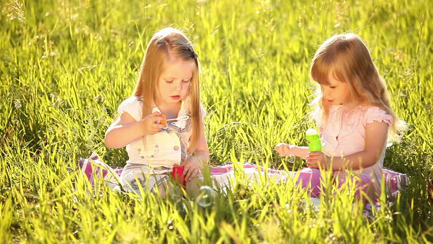 Two sisters blow bubbles in the meadow. 