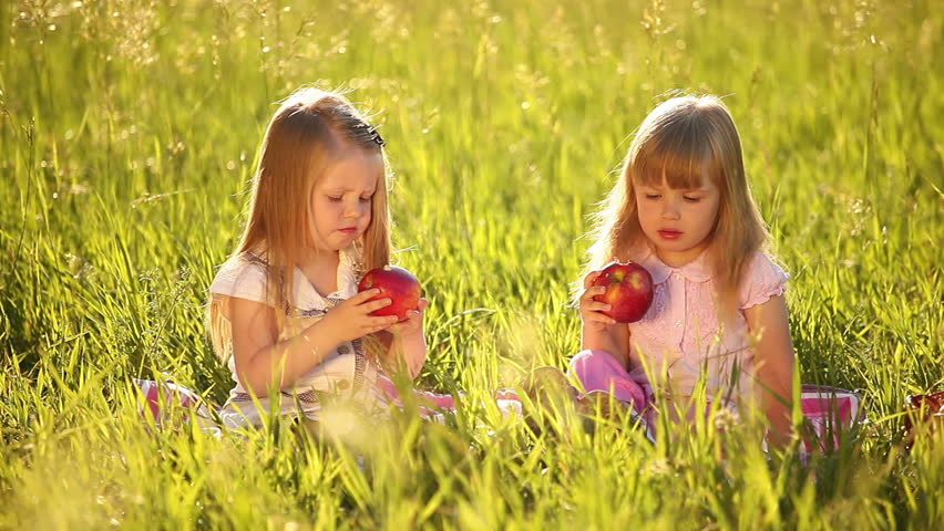 Two sisters eating apples in the meadow. Beside a basket of apples. 