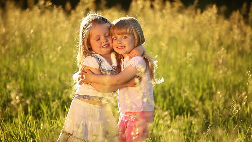 Two sisters embrace. Look at camera. They play in the meadow. 