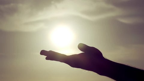 Grasping the sun with palm/fingers slow motion.100fps-25fps conformed slow motion shot of a silhouetted male hand against a sun and sky background, grasping the sun and letting sunlight pass through.