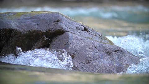 Water in the beautiful mountain river flows round a big stone in slowmotion