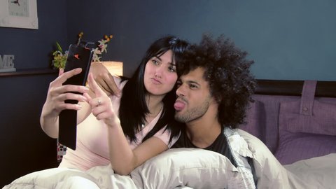 Happy couple taking selfie with cell phone at home making funny faces