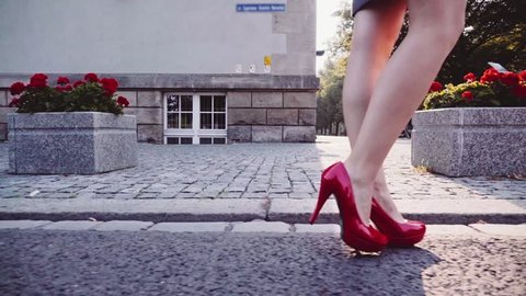 Sexy woman legs in red high heels shoes walking in the city urban street. Steadicam stabilized shot in Slow motion. Lens flare. Female legs in high-heeled shoes in the morning street.
