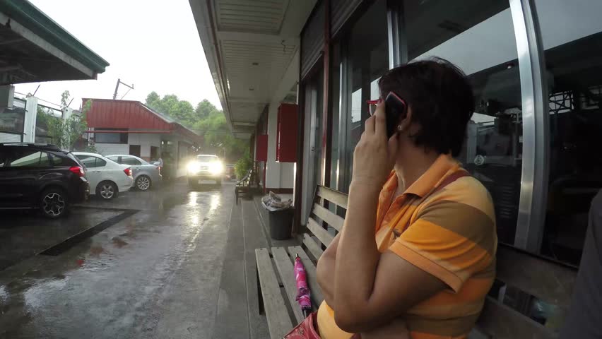Mature woman calling with the use of mobile smart-phone while in a car wash garage