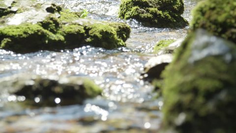 SLOW MOTION CLOSE UP: Spring river flowing between the mossy rocks