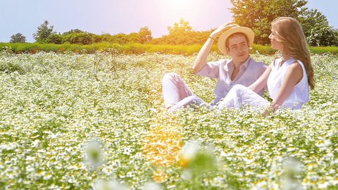 Happy, young romantic couple sitting in a chamomile daisy flowers field and have a fun.Slow motion, high speed camera, lens flare