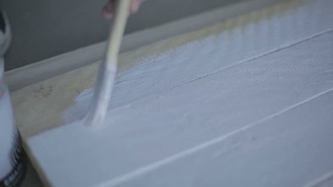 Man uses white paint to paint a wooden deck