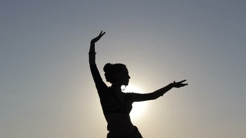 Silhouette girl oriental dancer masterly performing a dance on sky background