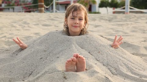 little girl with wet hair smiles siting filled up with sand on neck on beach