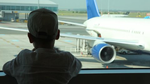 silhouette of boy close up looks through window at planes at airport