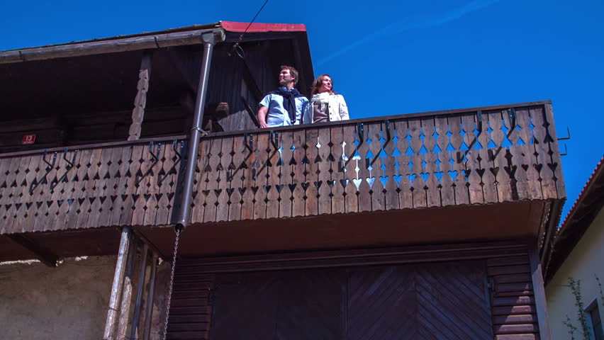 Couple standing on the balcony at the wooden vintage house and looking at the view over the countryside .