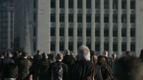 Slow motion of a large crowd of anonymous people in front of grey building in 4K. Large crowd of commuters and pedestrians walk across London Bridge to the City of London. Framed for graphics.