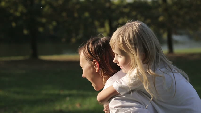 Daughter riding on mother in a city park at sunset. Slow motion Royalty-Free Stock Footage #12096125