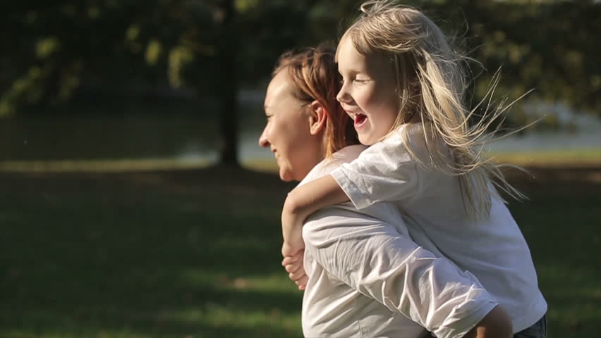 Daughter riding on mother in a city park at sunset. Slow motion Royalty-Free Stock Footage #12096125