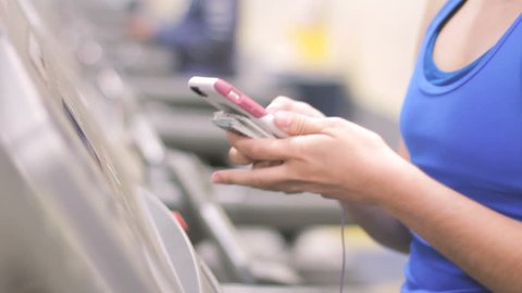 Young woman hands using smartphone to text message while walking on gym treadmill 