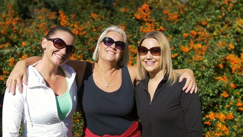 Mature Woman with Two Younger Women Smiling for Camera in Nature. Grey Haired Lady with Blond and Brunette Young Ladies Posing on Sunny Day