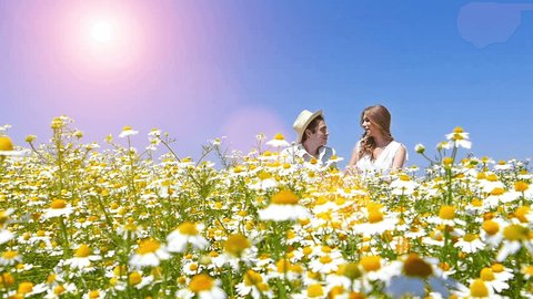 Happy, young smiling couple enjoying in a chamomile daisy flowers field.Slow motion, high speed camera, lens flare